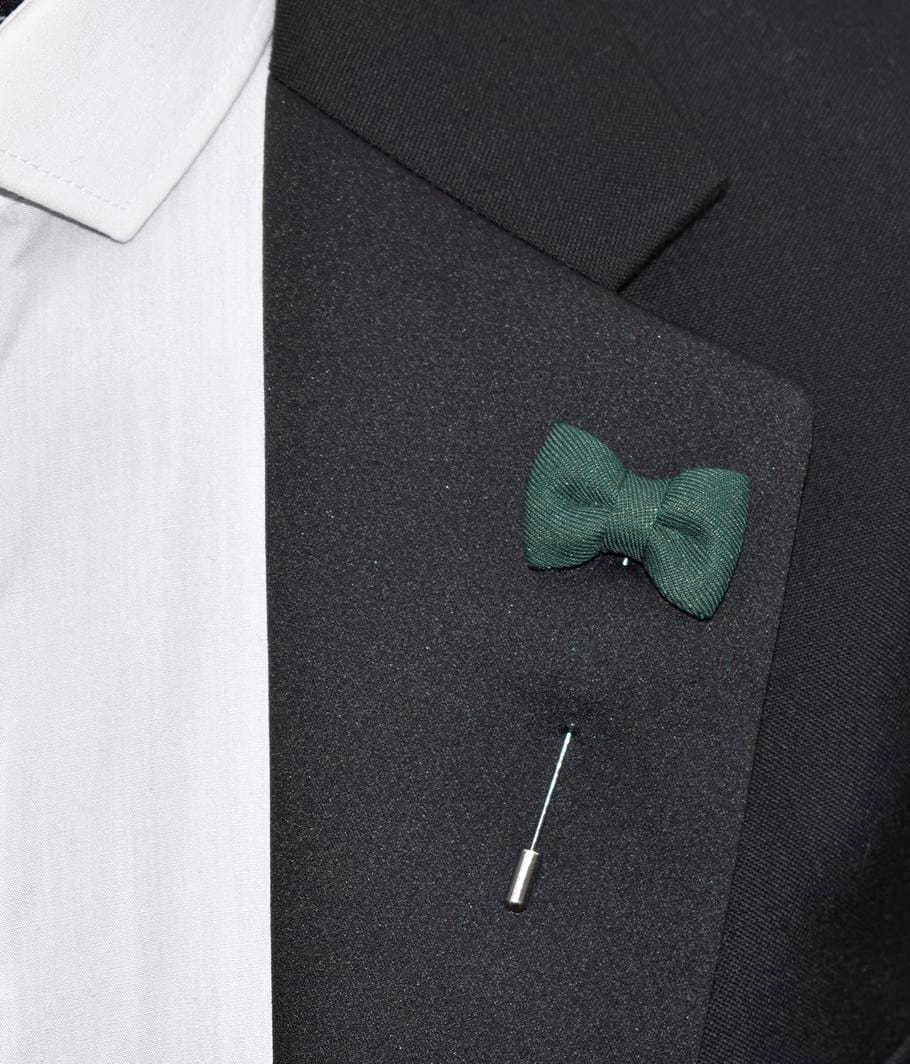 Green bow tie pin on a dark suit lapel with a white shirt collar.