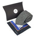 Gift set featuring grey herringbone tie, printed silk pocket square with mix of grey, black, orange and blue. and a silver tie clip, with large black presentation box behind it