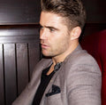 Man in a gray blazer sitting in a red chair with a dark wooden panel background