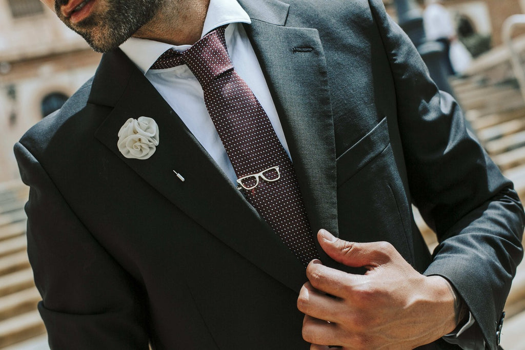 Man adjusting his suit jacket with a decorative lapel pin and tie.