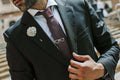 Man adjusting his suit jacket with a decorative lapel pin and tie.