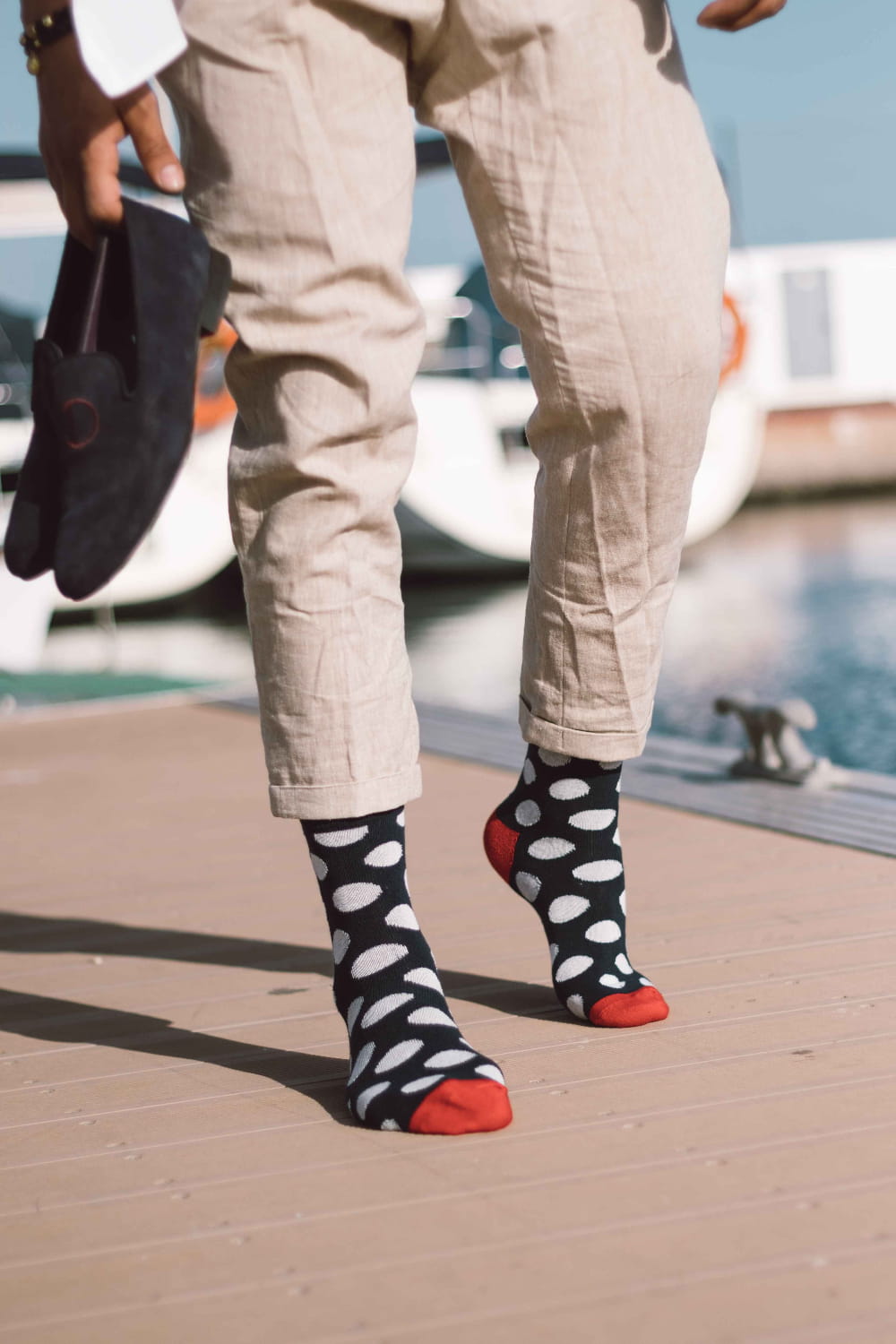 Person wearing beige pants and polka dot socks with red toes by a poolside.