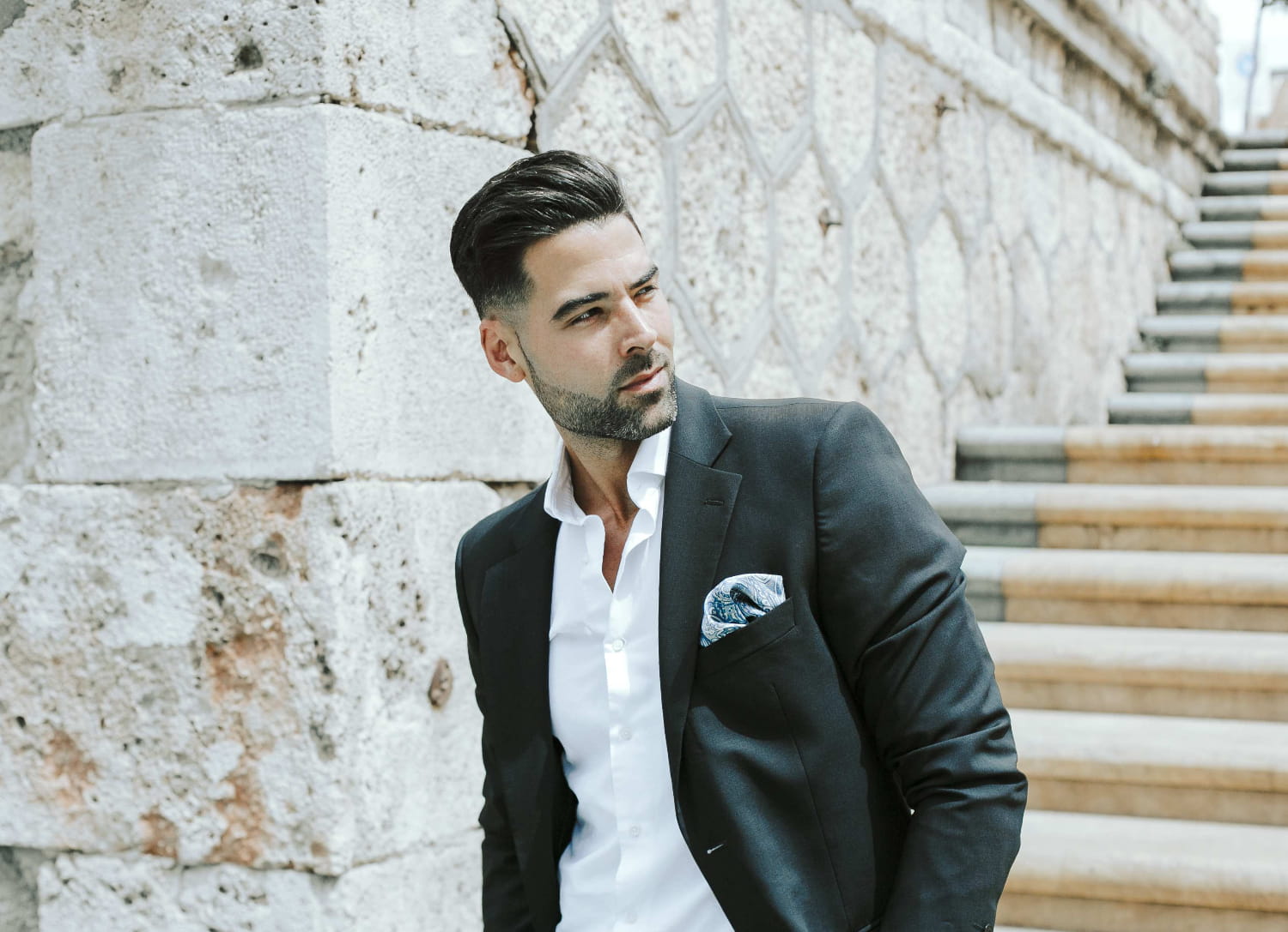 Man in a suit standing on stone steps with a stone wall background