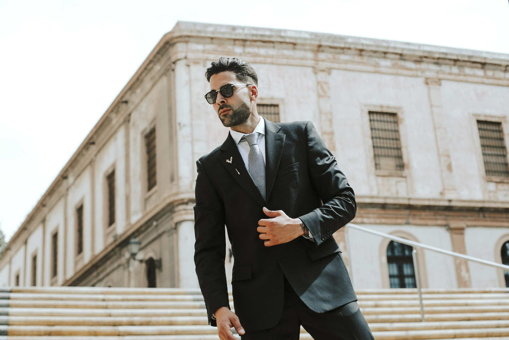 Man in a black suit and sunglasses standing in front of an old building