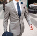 Man in light grey suit wearing a blue polka dot tie and blue lapel pin with a burgundy pocket square