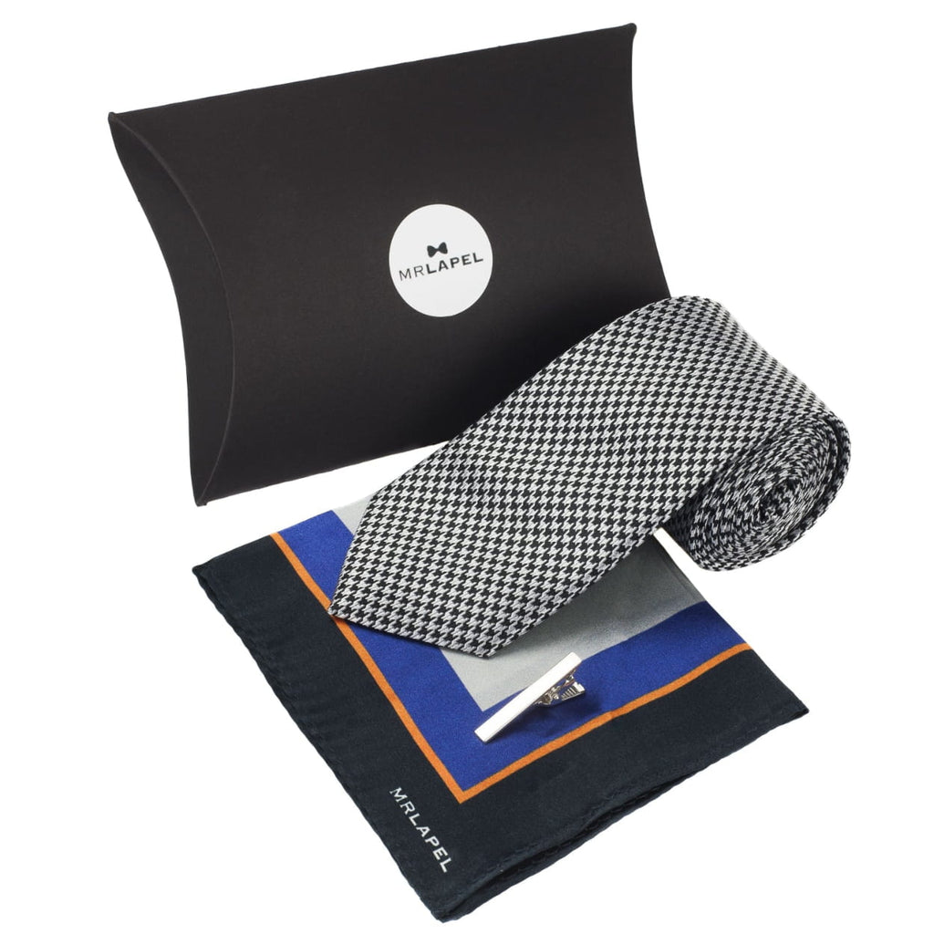 selection of men's gifts presented as a gift set, including a silver tie, a pocket square with black, orange, blue and grey motif, and a silver tie clip