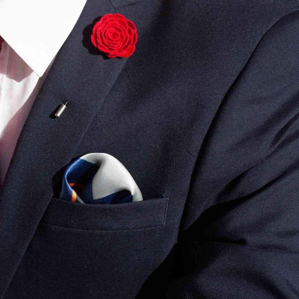 Navy suit jacket with a red flower pin on the lapel and a colorful pocket square.
