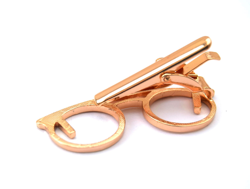 Rose gold tie clip in the shape of glasses on a white background