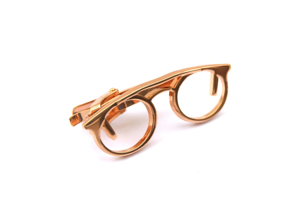 Rose gold tie clip in the shape of glasses on a white background
