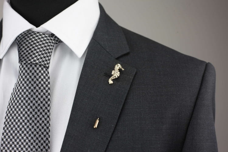 Gray suit jacket with a white shirt, patterned tie, and decorative seahorse pin on a neutral background